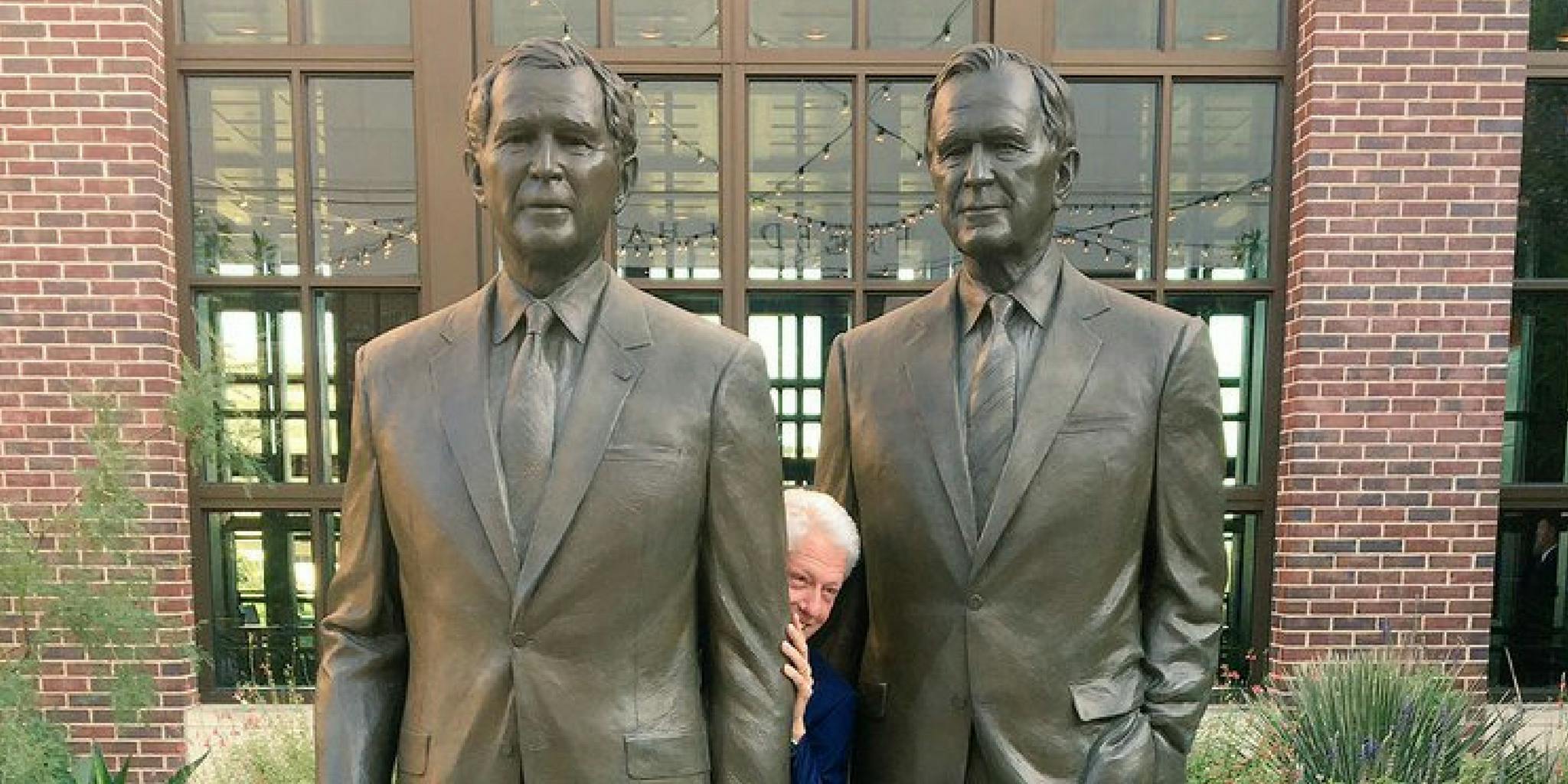 Bill Clinton hiding between statues of the Presidents Bush