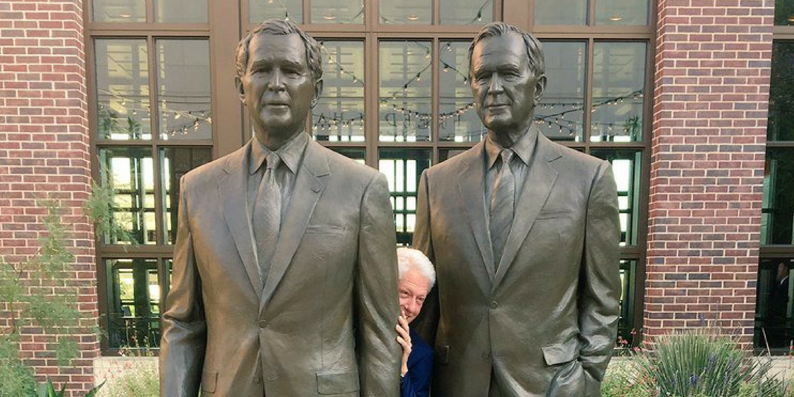 Bill Clinton hiding between statues of the Presidents Bush