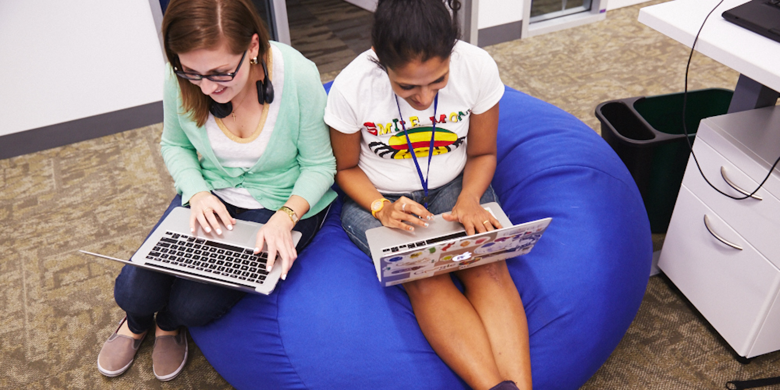 Googlers at work, two women working on laptops on a beanbag chair