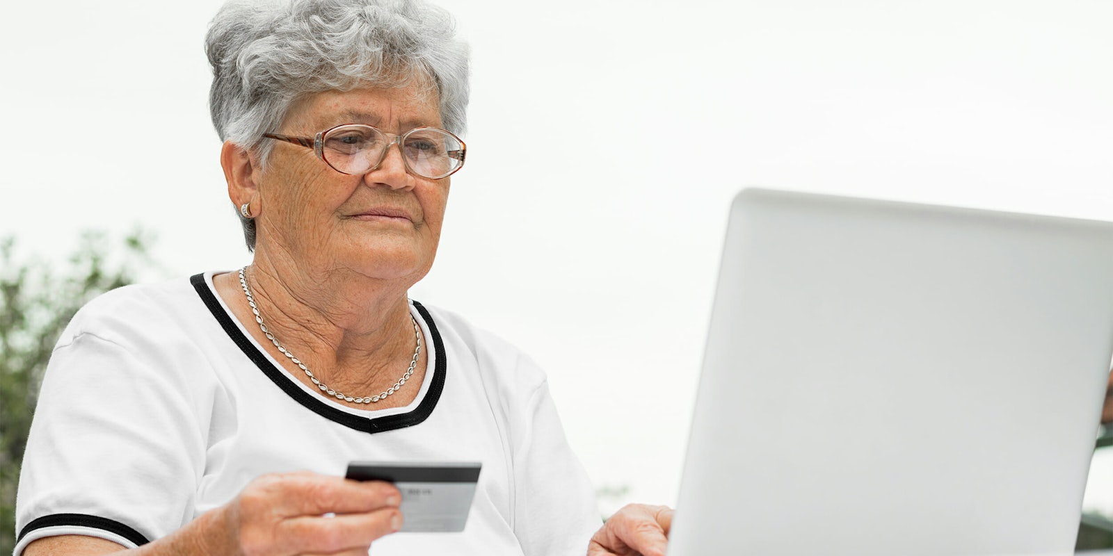 Elderly woman holding credit card while using laptop