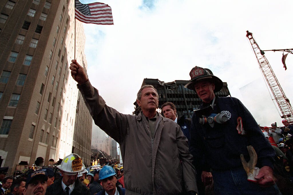 Standing atop rubble with retired New York City firefighter Bob Beckwith Friday, Sept. 14, 2001, President George W. Bush waves an American flag after addressing recovery workers in New York City. Photo by Paul Morse, Courtesy of the George W. Bush Presidential Library
