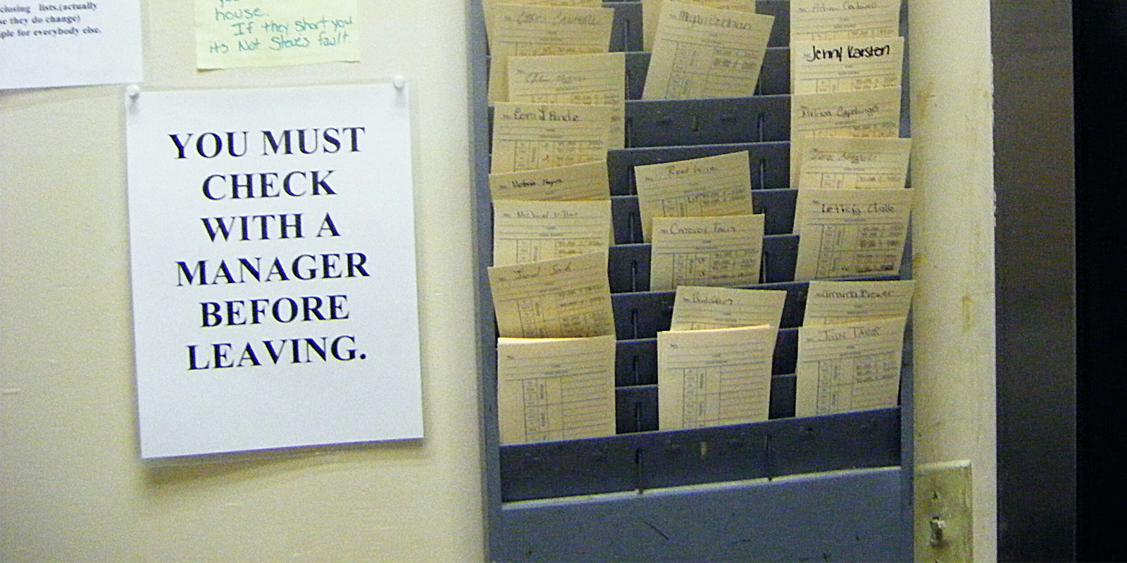 Timecards next to a sign that says 'You must check with a manager before leaving'