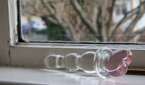 Image of a glass dildo sitting on a windowsill. 