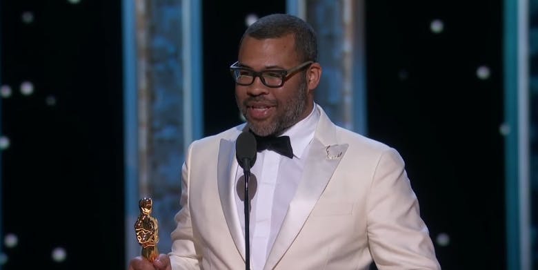 Jordan Peele giving his Oscars acceptance speech in a white tux and glasses