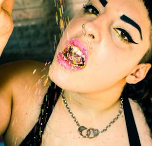 Close up of a performer pouring sprinkles into her mouth. 