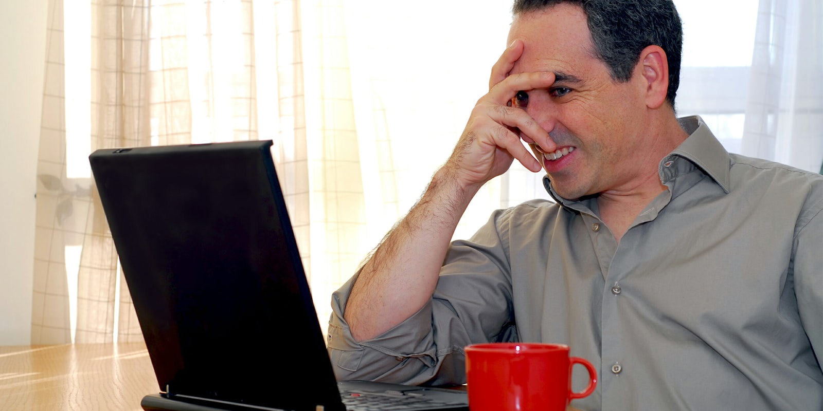 Man partially covering face while looking at laptop