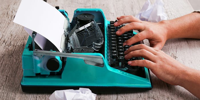 Man typing on blue typewriter with balled up sheets of paper on desk
