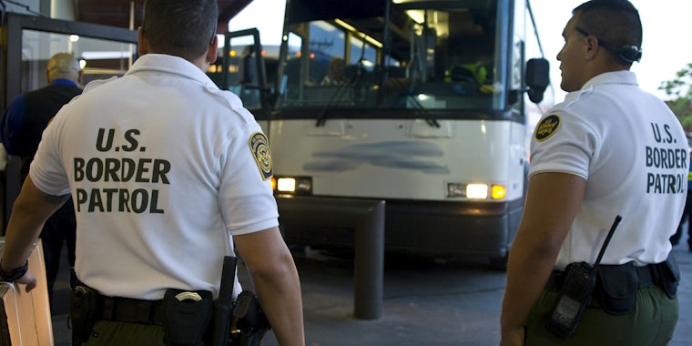 Customs officers await a greyhound bus for inspection in shirts reading: 'U.S. Border Patrol.'