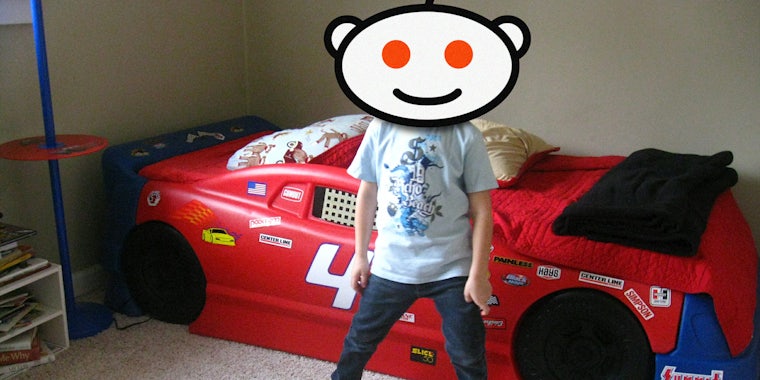 Child with Reddit Snoo head stands in front of race car bed