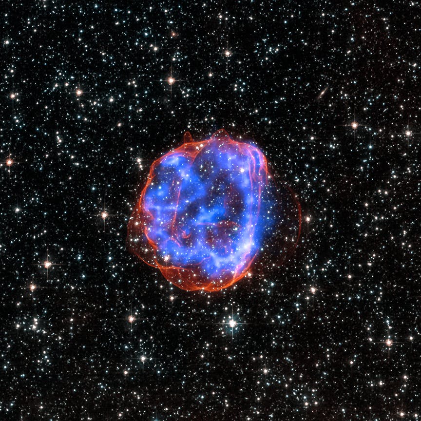 "SNR E0519-69.0: When a massive star exploded in the Large Magellanic Cloud, a satellite galaxy to the Milky Way, it left behind an expanding shell of debris called SNR 0519-69.0. Here, multimillion degree gas is seen in X-rays from Chandra (blue). The outer edge of the explosion (red) and stars in the field of view are seen in visible light from Hubble."