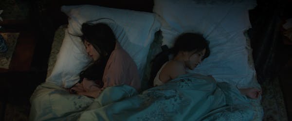 Two women lie back-to-back in a scene from The Handmaiden