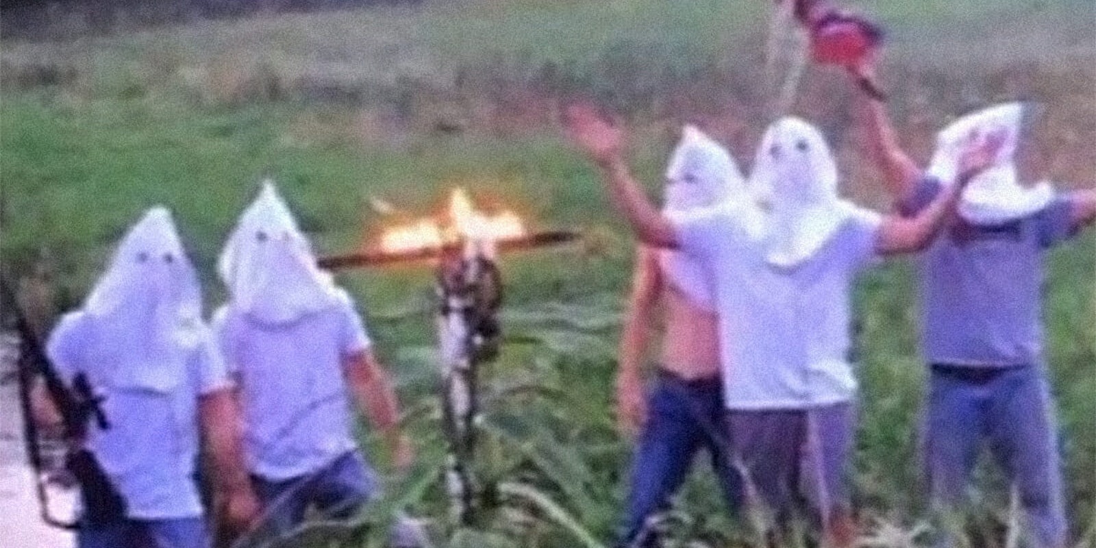 High school students in KKK regalia posing with rifle, burning cross, and confederate flag